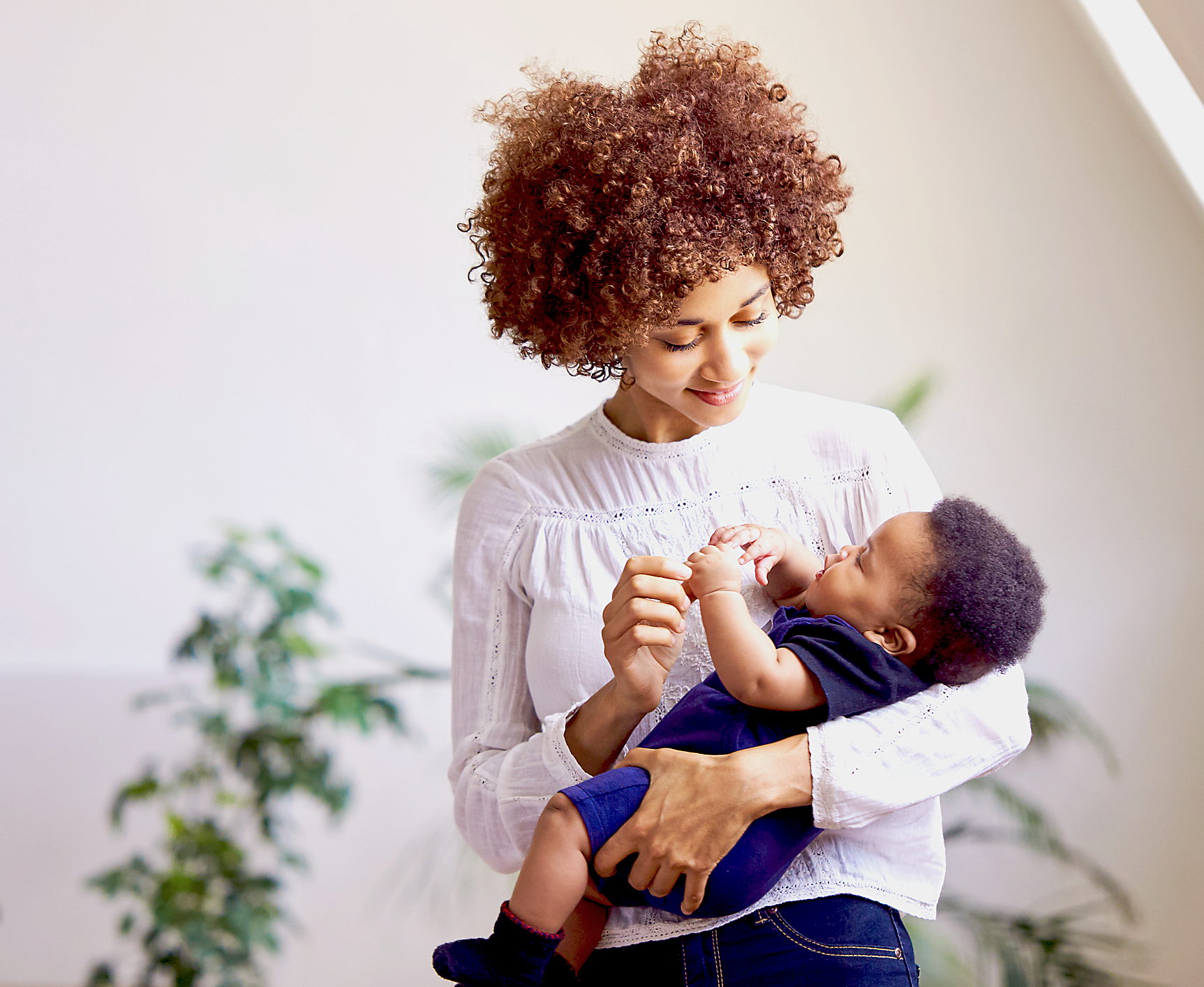 A young mom holds her baby in her arms while smiling at him.