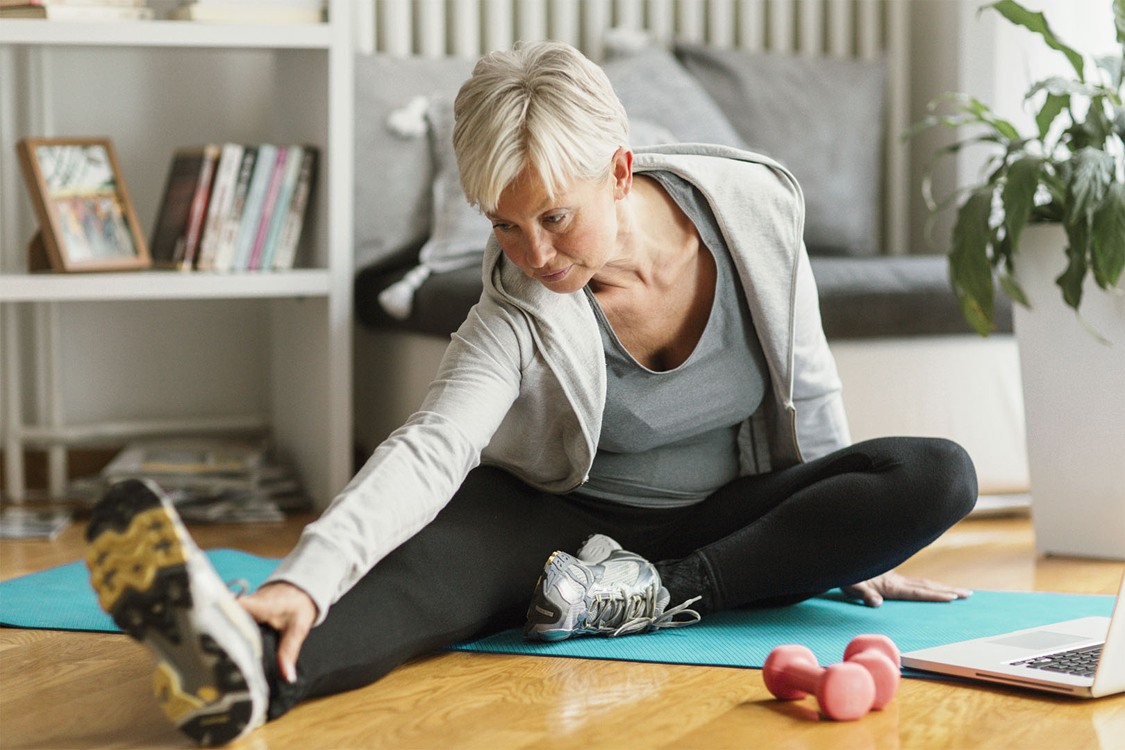 An older woman stretches on a mat on the floor of her home.