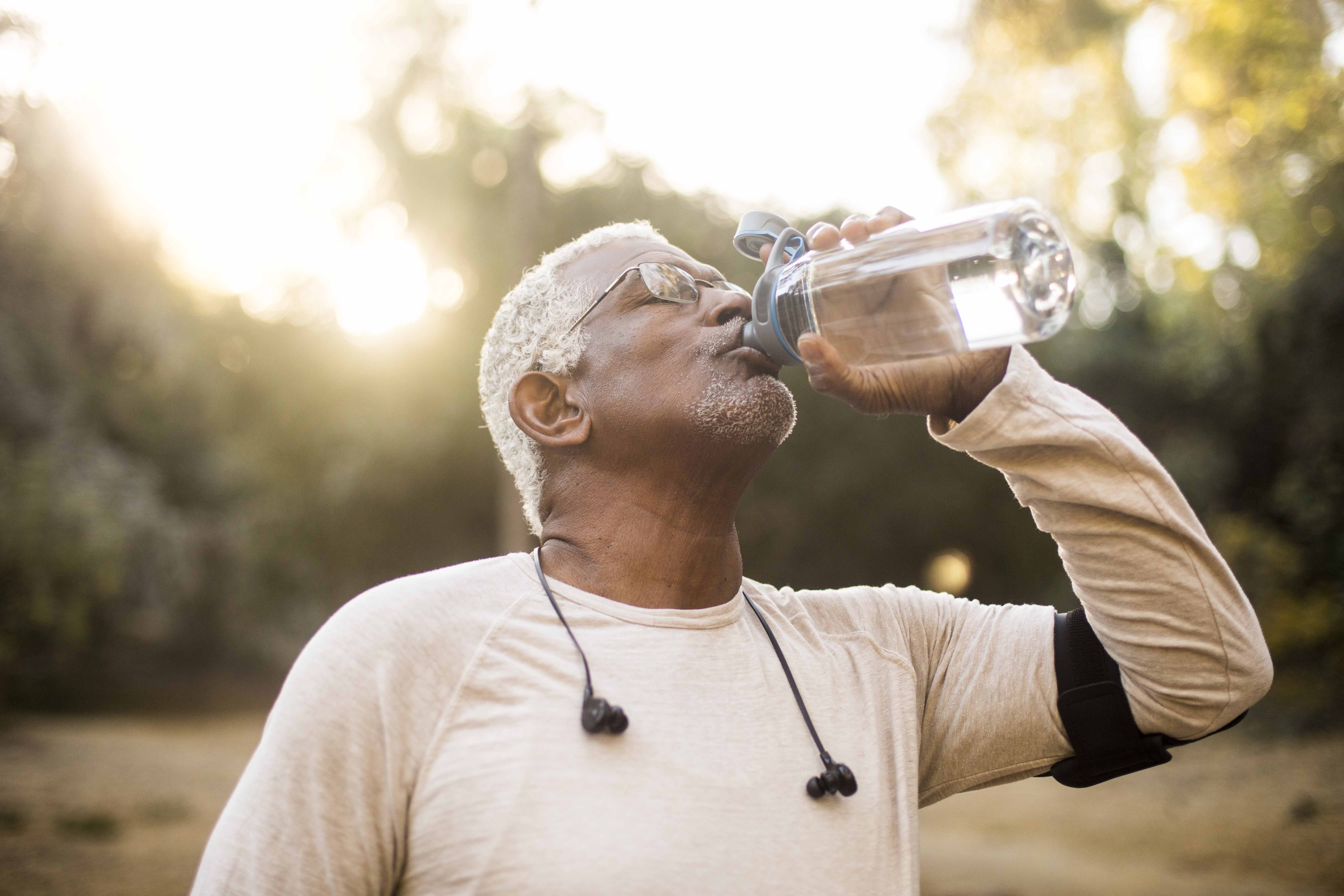 An older man takes a swig of water from his water bottle while enjoying the outdoors.