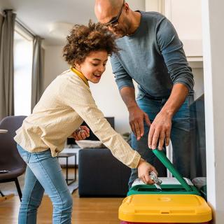 A father and his young daughter sort trash into bins in their home.