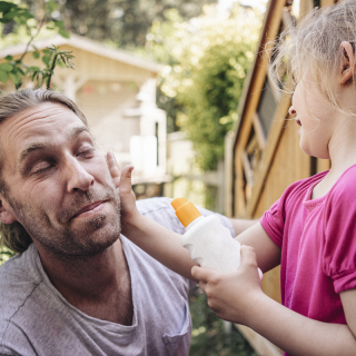 Child applying sunscreen to adult’s face to protect against UV rays